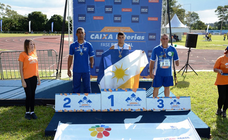 No lugar mais alto do pódio, o paratleta exibe, orgulhoso, a medalha de ouro e a bandeira do Tocantins